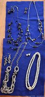 All five necklaces and three pairs of earrings laid out on blue cloth