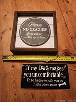 Two novelty wall signs with measuring tape for scale