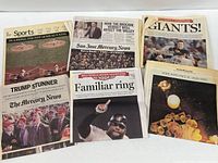 Group shot of seven folded newspapers showing all headline pages