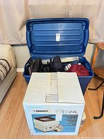 Blue plastic tote open with assorted camping gear visible beside boxed toilet