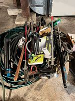 Pile of hoses and assorted hand tools including loppers, shears, broom head