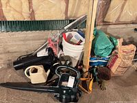 Overall view of garden tools pile with Craftsman leaf blower, watering can, bucket, tarp, soil and Quikrete bags