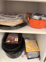 Shelved grouping showing sealed foil pans, orange colander with steamer, roaster stack and mitts