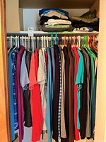 Closet rod with multiple women’s tops on hangers and folded pants on shelf