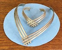 Choker necklace and cuff bangle laid flat on blue background showing matching four-bar design