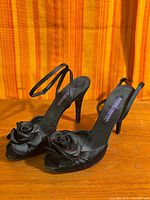 Full view of both black slingback sandals showing rosette toe detail and stiletto heels