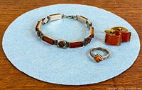 Bracelet, ring and cufflinks arranged on blue felt, showing overall design and amber stones