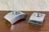 Pair of curved chrome candlestick holders on wood surface
