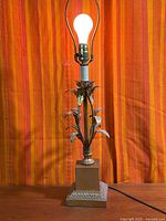 Full view of lit floral gilt metal table lamp on square base