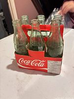 Front view of six green glass Coca-Cola bottles in red cardboard carrier
