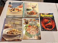 Front covers of all five softcover cookbooks arranged on table