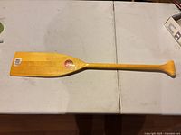 Full view of varnished wood canoe paddle showing shaft, blade and handle