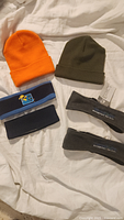 All six items laid out on bedding: orange and khaki toques, blue fleece headband, navy headband, two grey fleece headbands