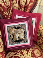 Two burgundy elephant pillow covers on patterned chair