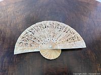 Full view of opened carved ox bone fan on tabletop