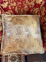 Front view of square gold paisley brocade pillow on patterned chair