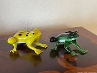 Yellow and green Murano glass frog figurines on wood surface