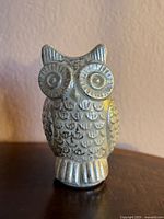 Front view of metallic silver owl figurine on flat surface