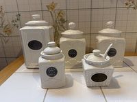 Group view of all five white ceramic canisters showing sizes and silver plaques