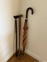 All three items leaning in corner: striped umbrella, black cane, wood cane