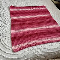 Full view of pink striped crocheted afghan laid flat on mattress
