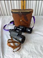 Binoculars beside brown leather hard case, purple strap visible