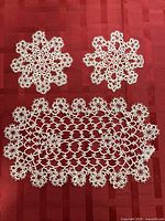 All three white hand-tatted doilies on red background
