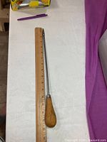 Full view of trussing needle beside ruler showing 0–15.5 inch length