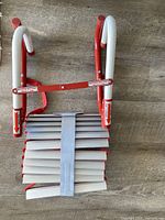 Top view of folded fire escape ladder showing red steel hooks and aluminum rungs