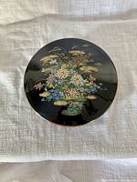 Top view of black round floral trinket box showing painted decoration