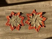 Two star-shaped beige and orange crochet doilies on wood surface