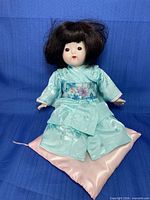 Full doll seated on pink satin pillow