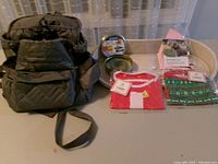 All items displayed together: backpack carrier, feeder tray, flea collar tin, packaged shirts and cap