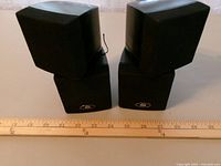 Front view of both speakers showing grille and logo with ruler for scale