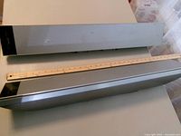 Front view of both slim silver speakers with yardstick for scale