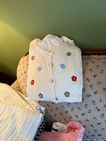 Folded white quilted cardigan with floral appliqués atop pile