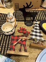 small tabletop decor items including ceramic snowman planter, buffalo plaid moose, plaid tree, black metal reindeer