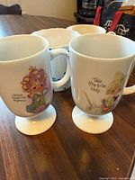Pair of Precious Moments pedestal mugs with sayings; third mug partially visible behind