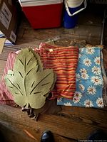 Stack of various folded table linens with green leaf placemats on wooden floor