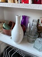 Shelf with white ceramic vase, purple glass vase, glassware and bowl