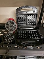 Both waffle makers open showing interior waffle plates: Black+Decker double-square, red Dash mini