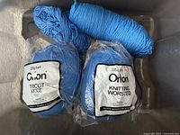 Two sealed blue Orlon yarn skeins and one loose skein in bin
