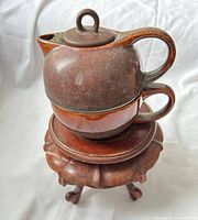 Teapot stacked on cup placed on wooden stand