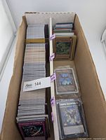 Full view of long storage box with two card rows, unsleeved stacks on left, sleeved/top-loaded cards on right