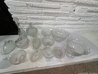 Group view of all pressed glass pieces including decanter, bowls, compotes, covered dishes and coasters