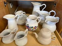Cabinet shelf showing all pitchers, teapot, cups and saucers