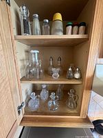 Cabinet interior showing three shelves of glass cruets, carafes, salt and pepper shakers and spice shakers