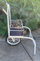 Side view of white metal garden cart holding blue planter box