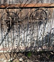 Full view of both iron arched trellises leaning against fence