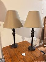 Two matching dark bronze metal table lamps with beige shades on wood table